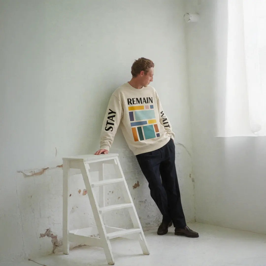 Male model wearing abstract color block sweatshirt with muted teal, mustard, rust and navy geometric print and the word REMAIN across the chest