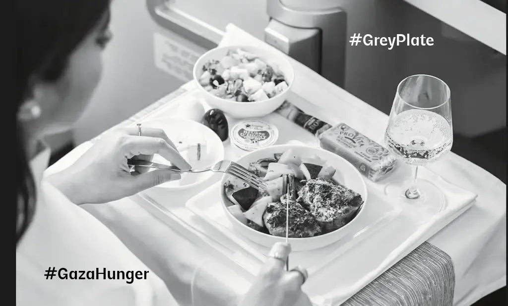 A greyscale photo of a woman dining on a luxury airline meal, with gourmet dishes and a glass of sparkling drink on a white tray table. The hashtags #GreyPlate and #GazaHunger are overlaid, highlighting the contrast between indulgence and crisis.