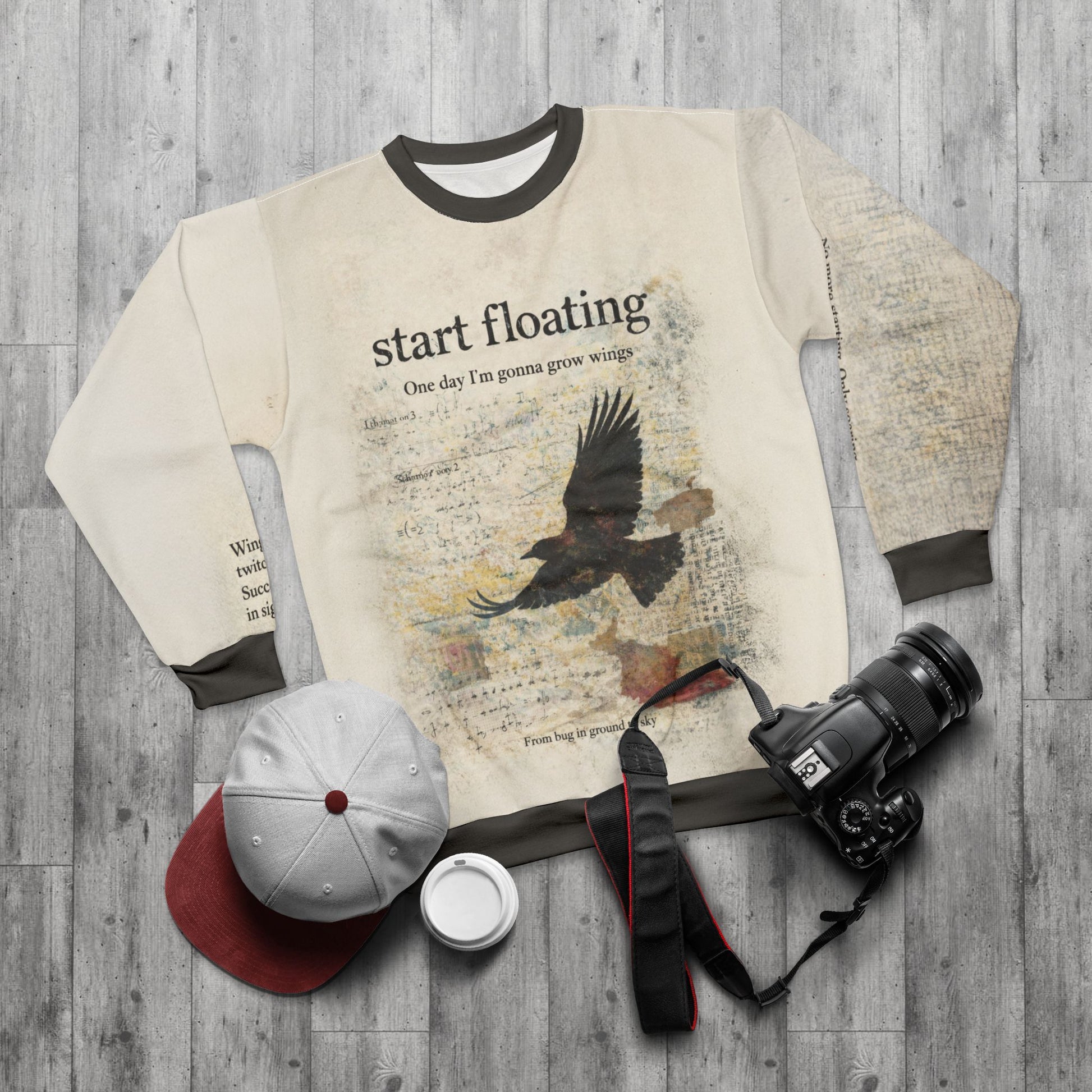 Dark academia raven graphic sweatshirt laid flat with vintage textures, styled with a camera and cap for an artistic lifestyle flat lay