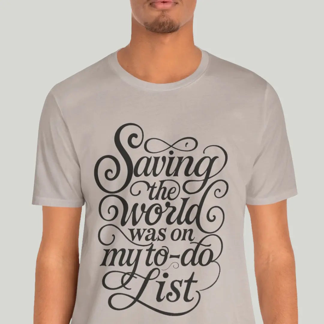 Person wearing a light gray t-shirt with black text "saving the world was on my to do list: design on a plain background