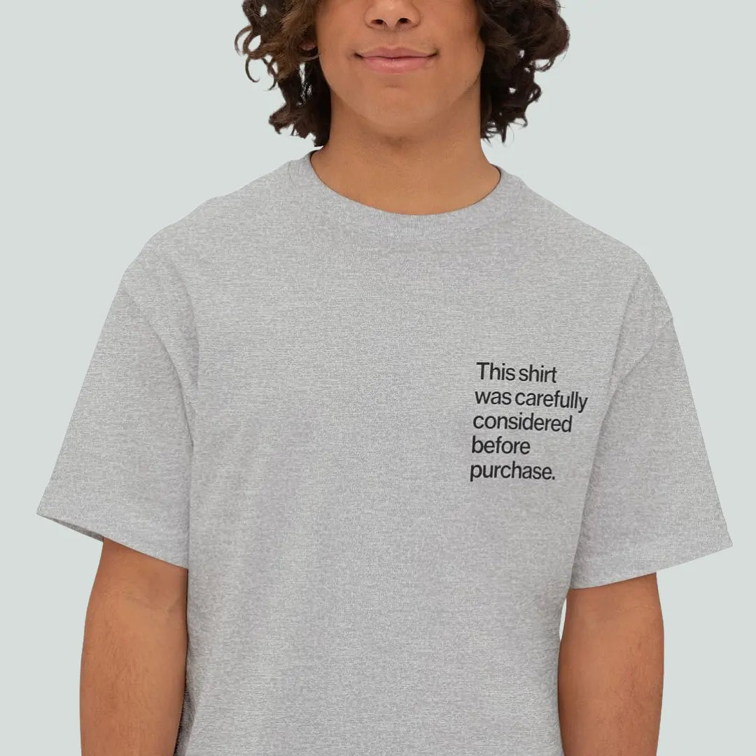 Person wearing a grey Introvert T Shirt with minimalist Helvetica left-chest text, reading this shirt was carefully considered before purchase