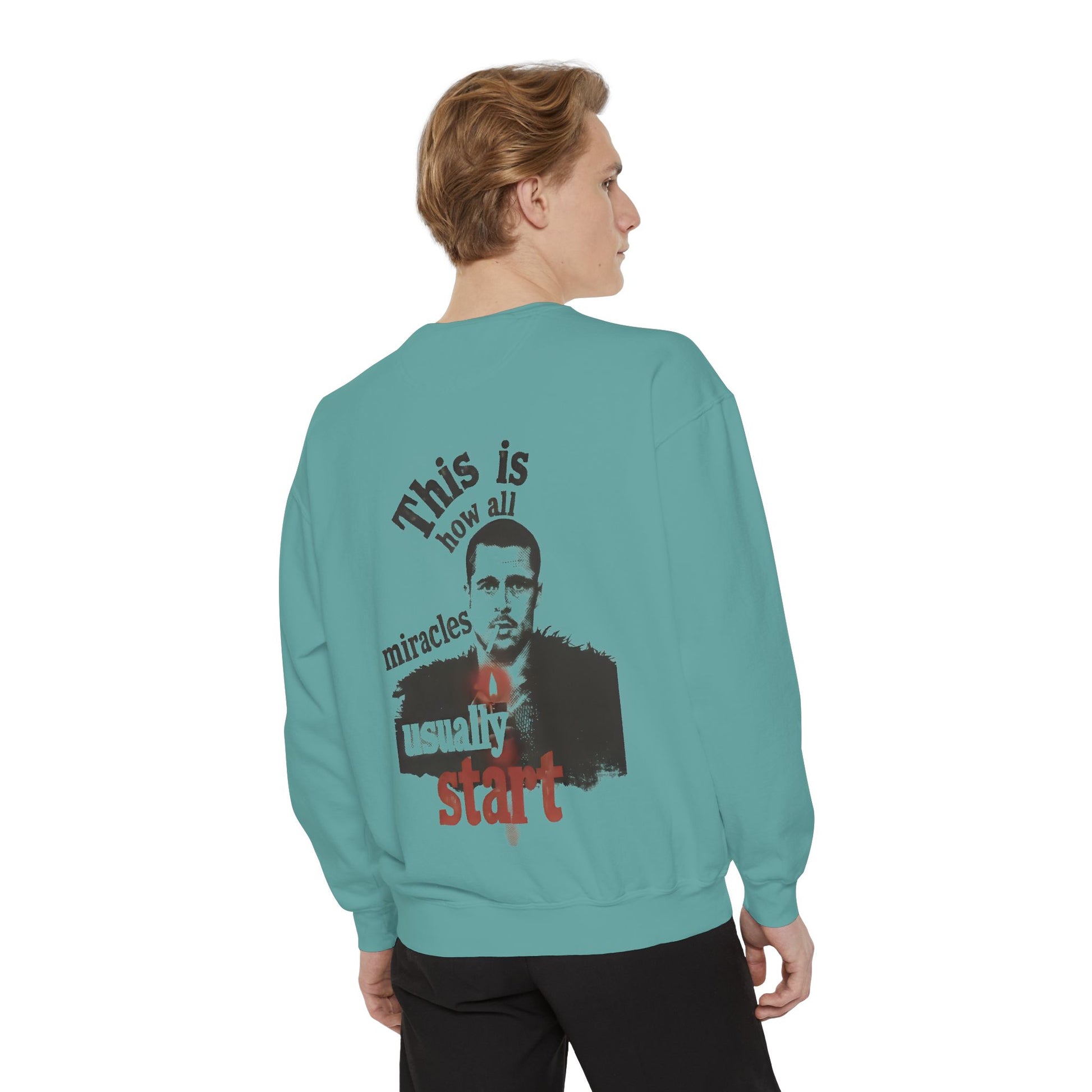 Person wearing a teal sweatshirt with brad pitt illustration and typography "this is how all miracles usually start"