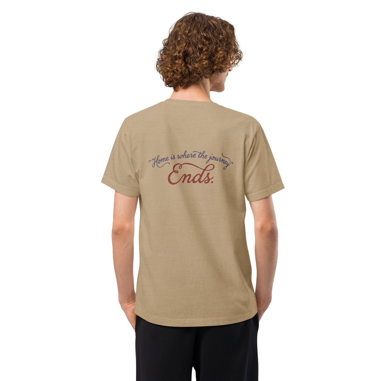 Back view of a model wearing a beige heavyweight streetwear T-shirt with a distressed handwritten script graphic reading “Home is where the journey ends,” in an oversized unisex, garment-dyed fit.