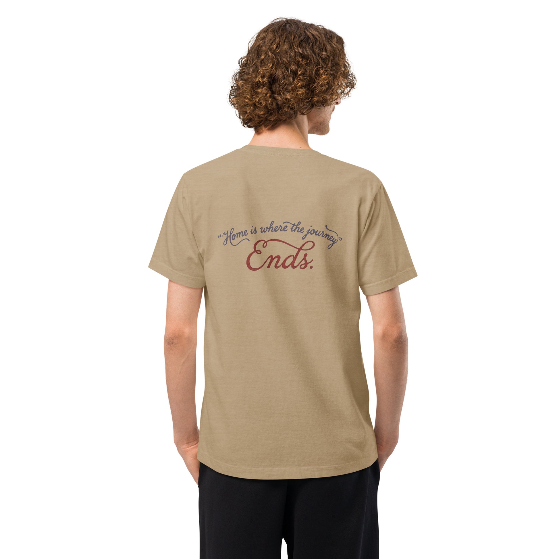 Back view of a model wearing a beige heavyweight streetwear T-shirt with a distressed handwritten script graphic reading “Home is where the journey ends,” in an oversized unisex, garment-dyed fit.